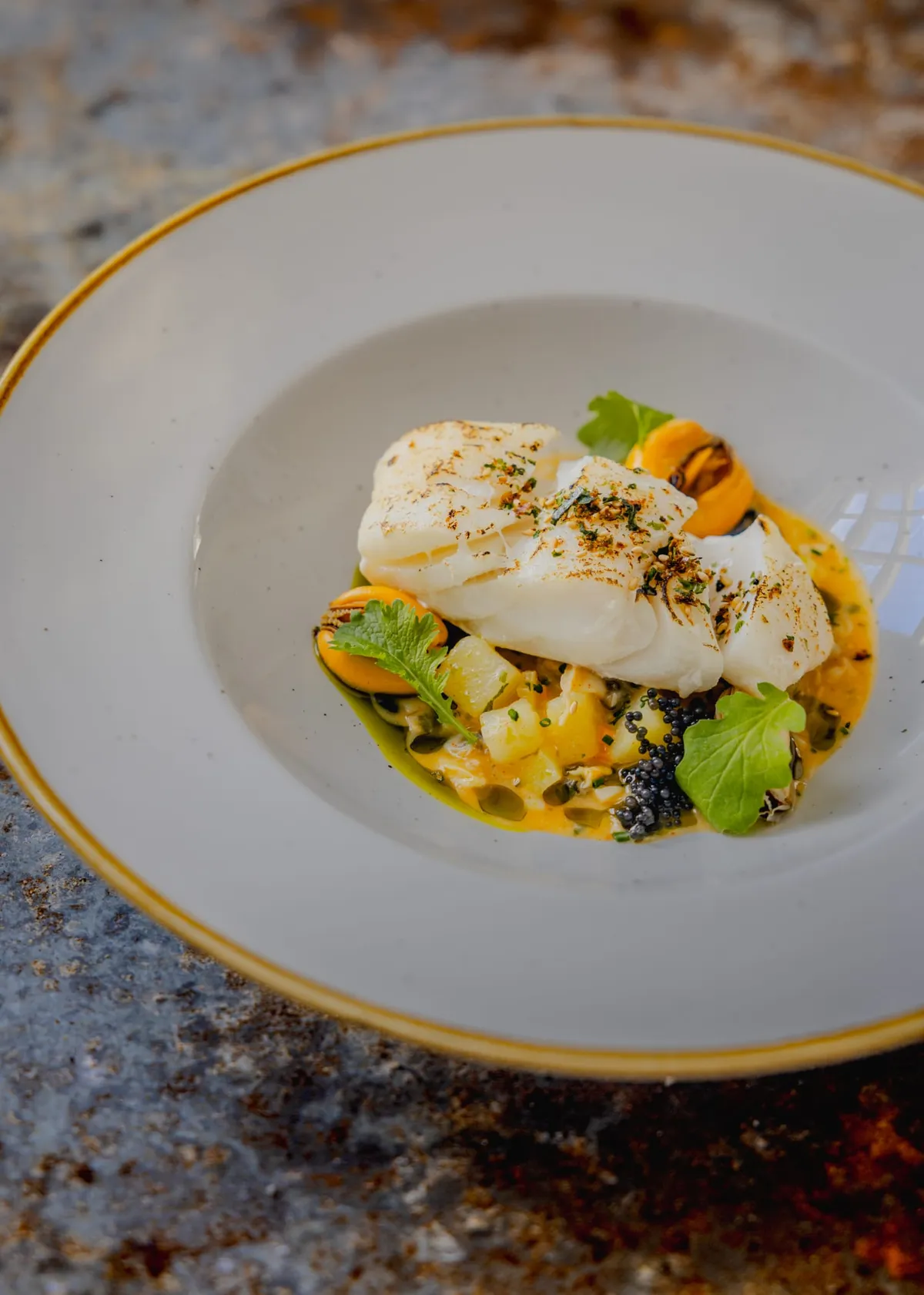 Cornish market fish with mussels, Tabiko and crushed potato in a clam and white miso chowder, on a speckled bowl