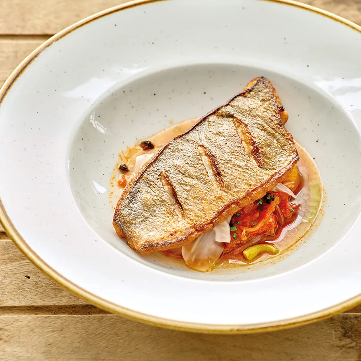 Crispy-skinned fish fillet on a tomato and pepper base, in a white speckled bowl