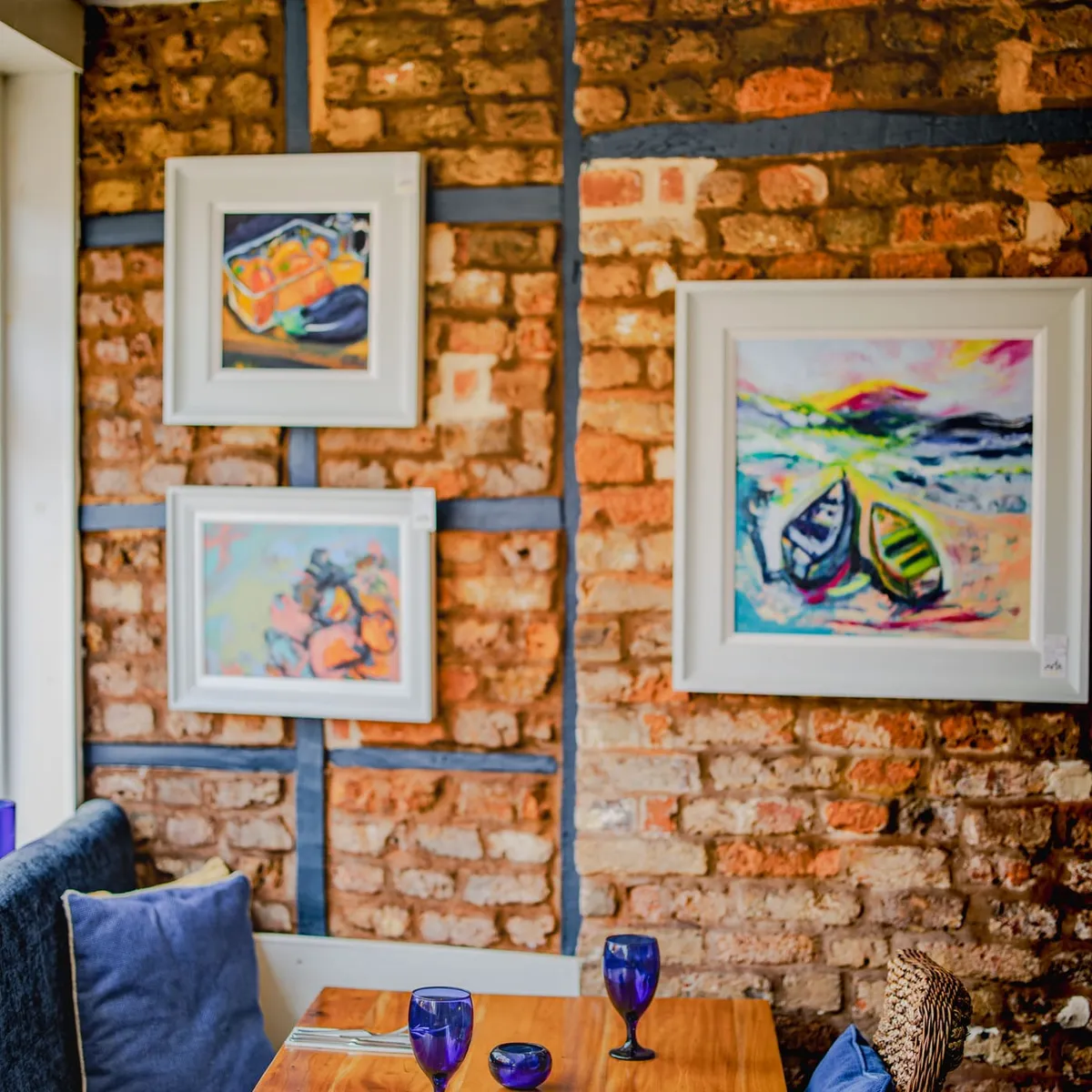 Local artwork on the exposed brick wall above a laid table in The Galley dining room