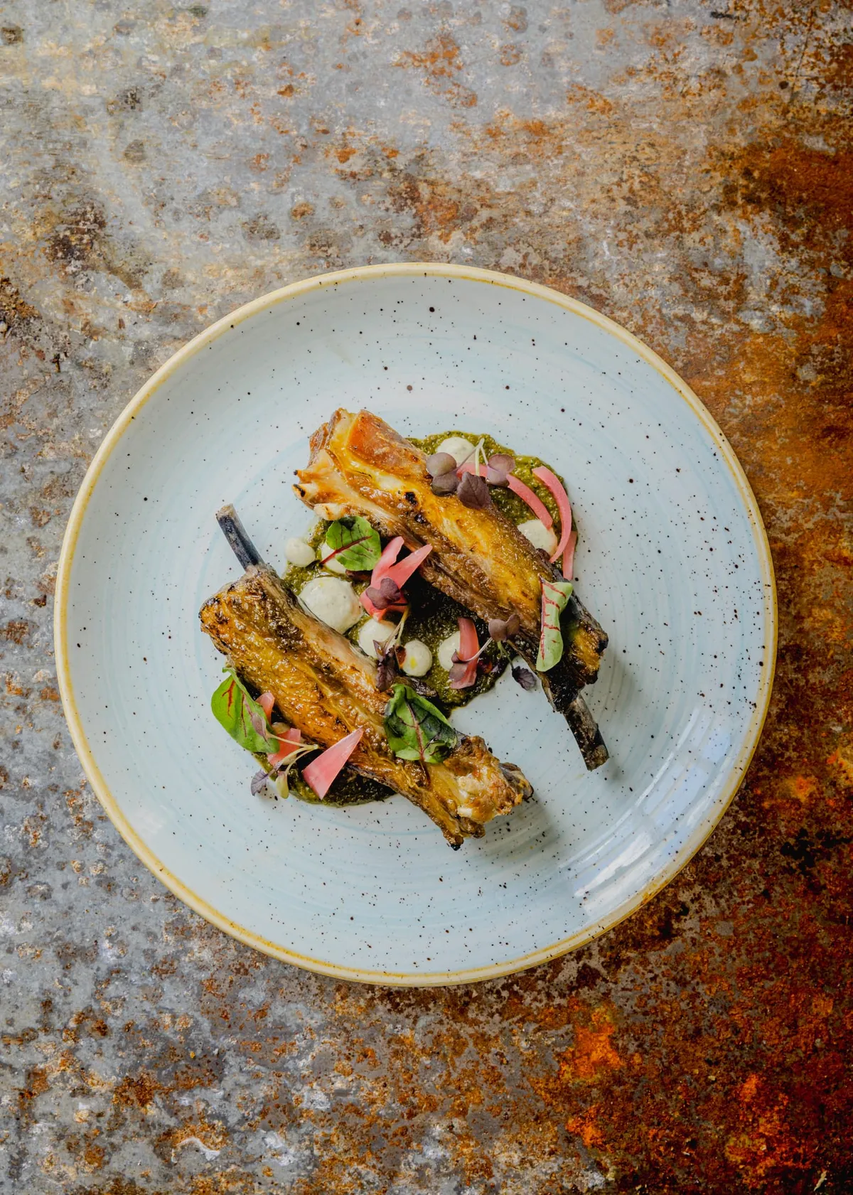 Glazed lamb ribs with pickled radish and herbs on a pale blue speckled plate