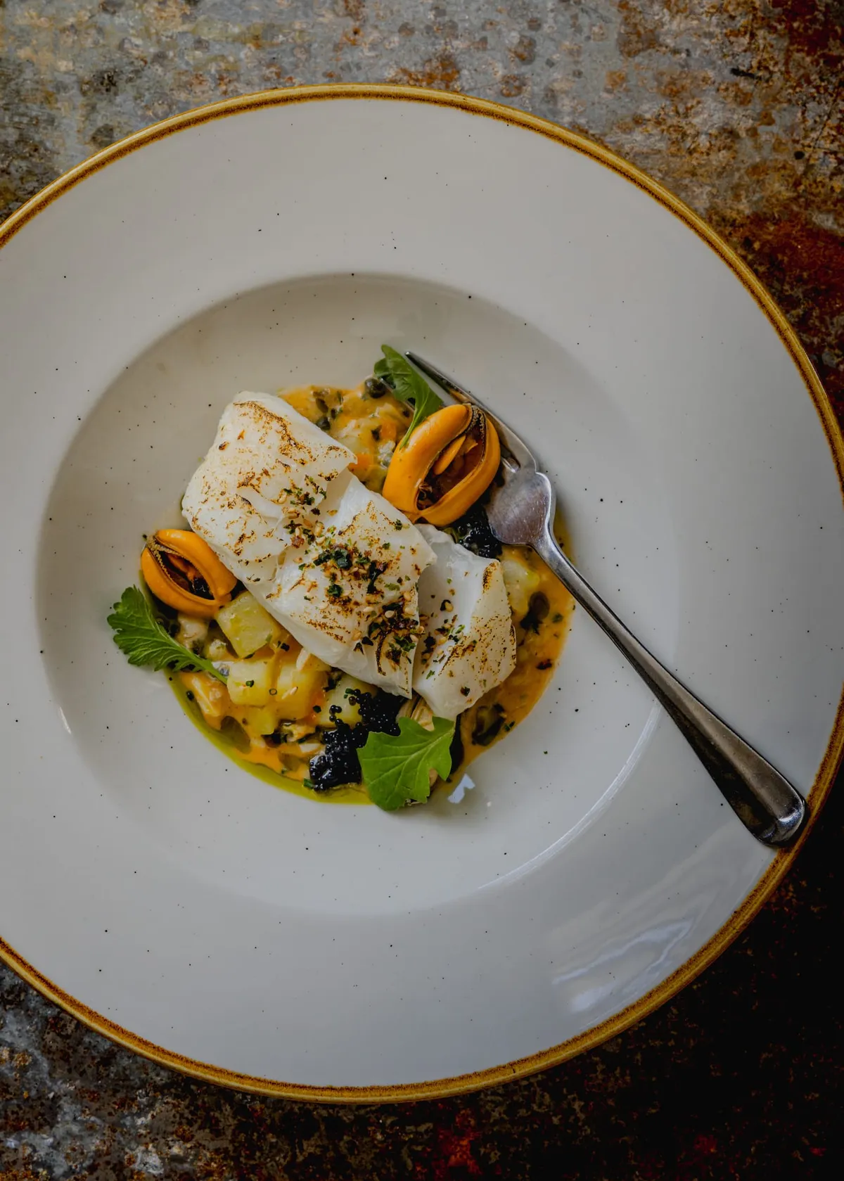 Cornish market fish on a clam and white miso chowder, top-down with a fork