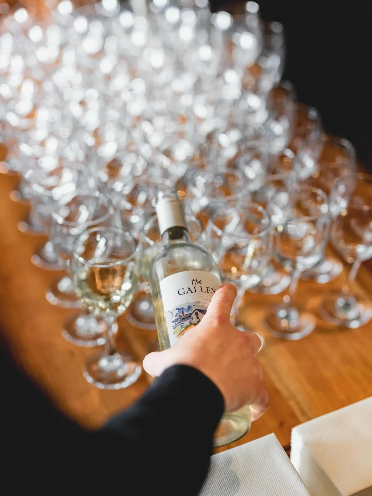 A bottle of The Galley house wine on the table at an event, rows of glasses ready